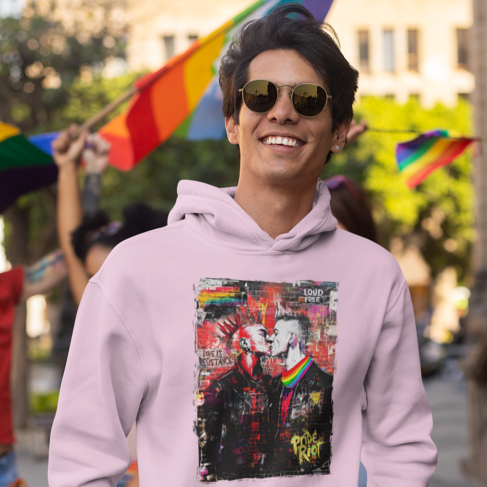 Person wearing a pink hoodie with a graphic design, standing in an outdoor setting with rainbow flags.