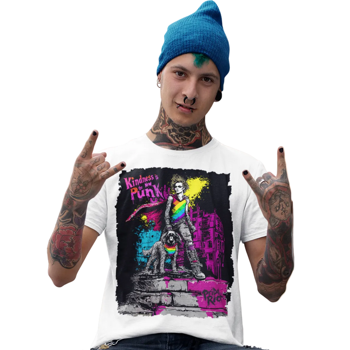 A man wearing a white graphic colorful Pride Riot tee, paired with ripped black jeans and a blue beanie, sitting on a concrete ledge in front of a building.