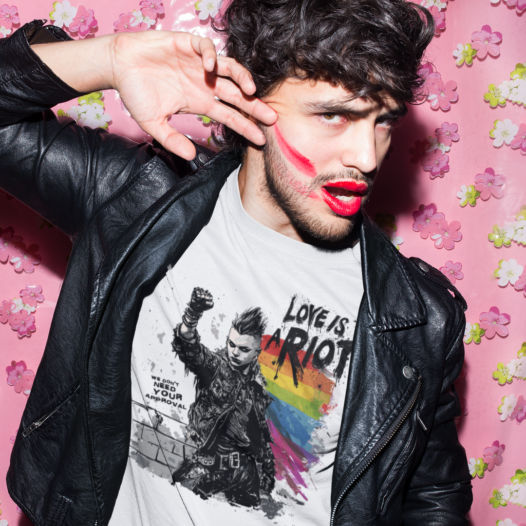 Pride Riot 'Love is a Riot' graphic t-shirt in soft white. Bold, distressed black text reads 'LOVE IS A RIOT' in a punk aesthetic. Inclusive fit streetwear on a non-binary model. Soft cotton fabric detail