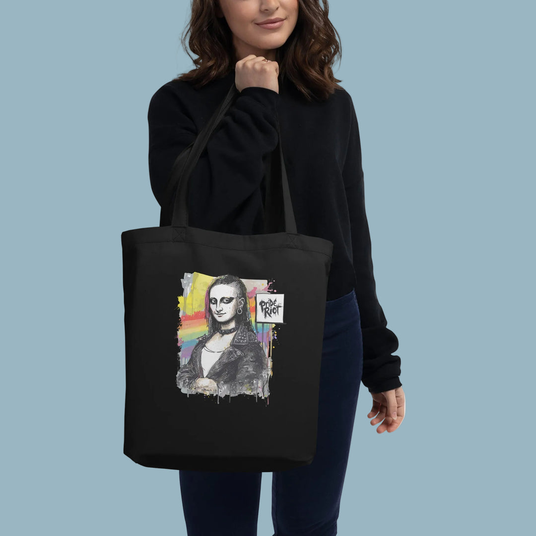 A model holding up a black heavyweight canvas tote bag featuring a punk rock version of the Mona Lisa. The art graphic is bold and subversive, reimagining classic art with a rebellious streetwear aesthetic. The bag is shown as a durable, high-capacity accessory suitable for daily use.
