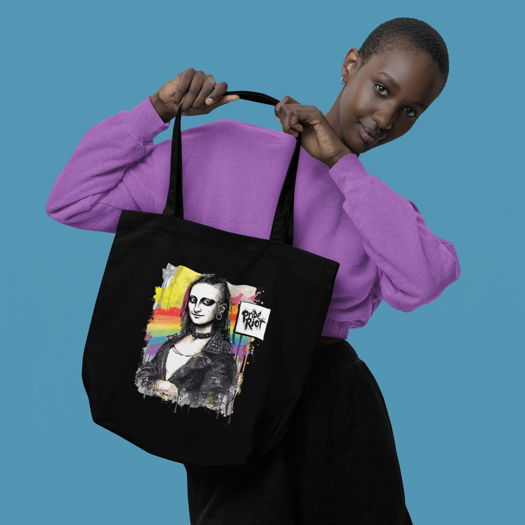 A model holding up a black heavyweight canvas tote bag featuring a punk rock version of the Mona Lisa. The graphic is bold and subversive, reimagining classic art with a rebellious streetwear aesthetic. The bag is shown as a durable, high-capacity accessory suitable for daily use.